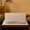 Beige clutch bag with striped pattern on a wooden surface against a beige wall.