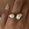 Gold rings with pearl-like stones on a hand against a neutral background