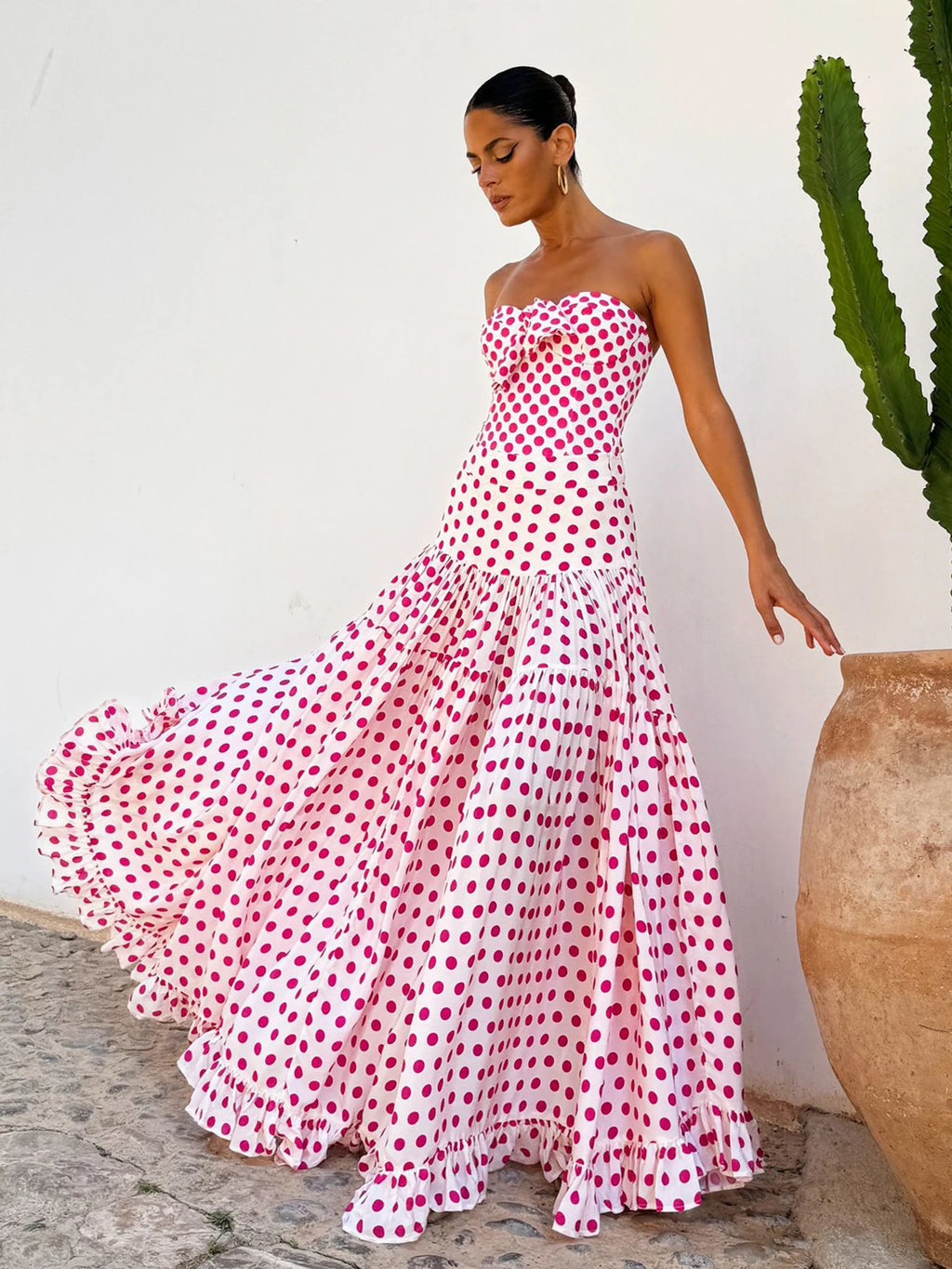Woman wearing a strapless polka dot dress standing next to a cactus plant.