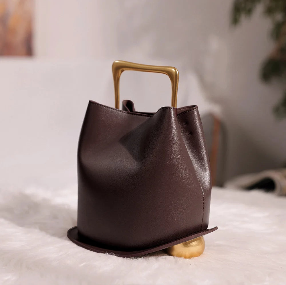 Brown leather handbag with gold handle and base on a light surface