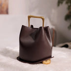 Brown leather handbag with gold handle and base on a light surface