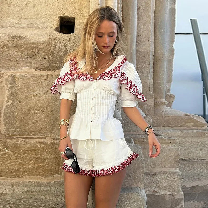 Woman in a white outfit with red embroidery standing against a stone wall.