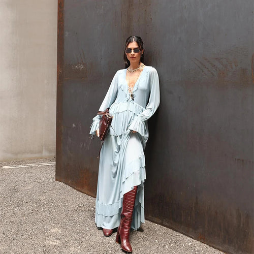 Woman in a light blue dress and red boots standing against a textured wall.