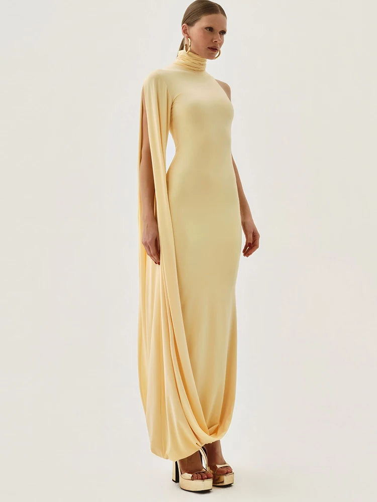 Woman wearing a long, light-colored dress with cape sleeves on a white background