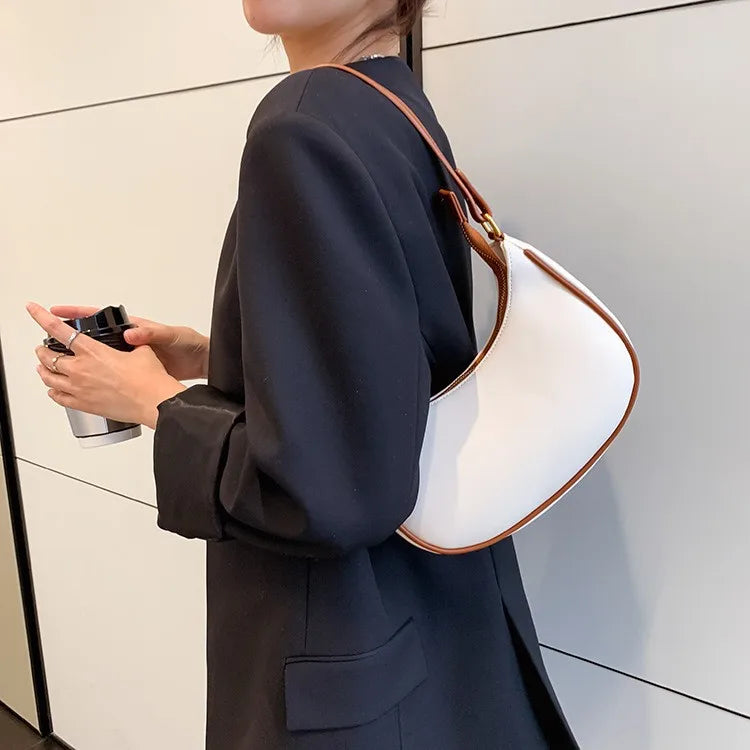 Person wearing a dark suit with a white handbag and holding a phone.