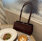 Brown leather handbag on a table with a dish and coffee cup.