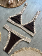 Black bikini with gold lace trim on a textured surface