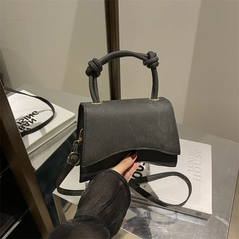 Black handbag with knotted handle held by a person, placed on a magazine.