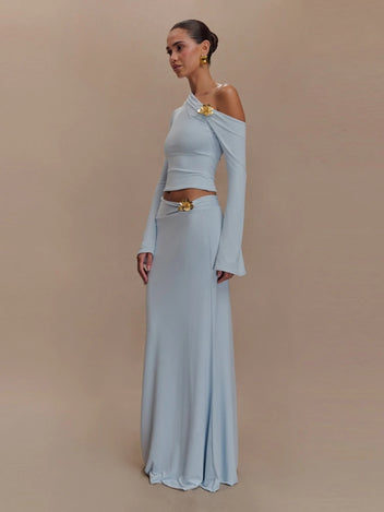 Woman wearing a light blue off-shoulder top and long skirt with gold accents on a beige background