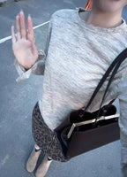 Person wearing a gray sweater and leopard print pants, holding a black handbag outdoors.