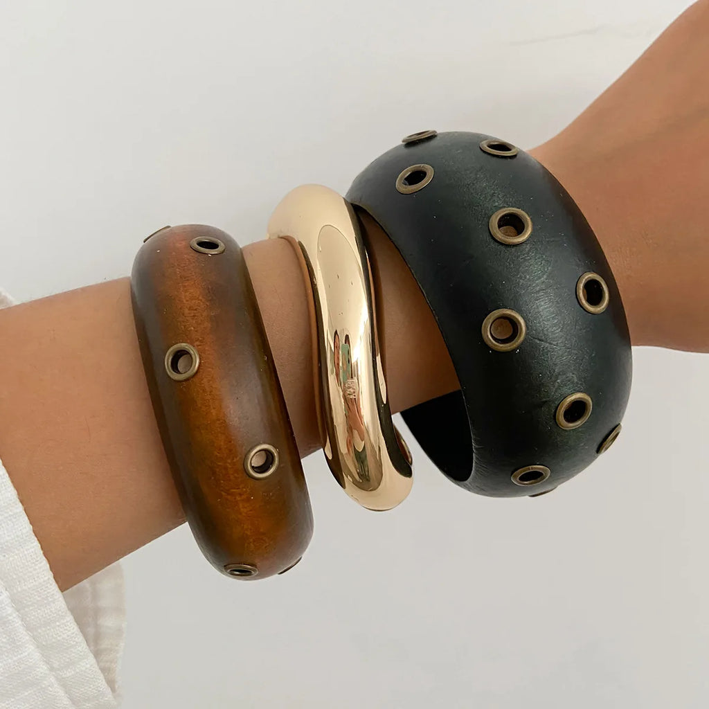 Three bracelets in brown, gold, and black on a wrist against a white background