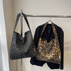 Two tote bags with leopard print design hanging on a rack.