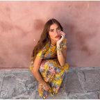 Woman in a floral dress sitting against a pink wall.