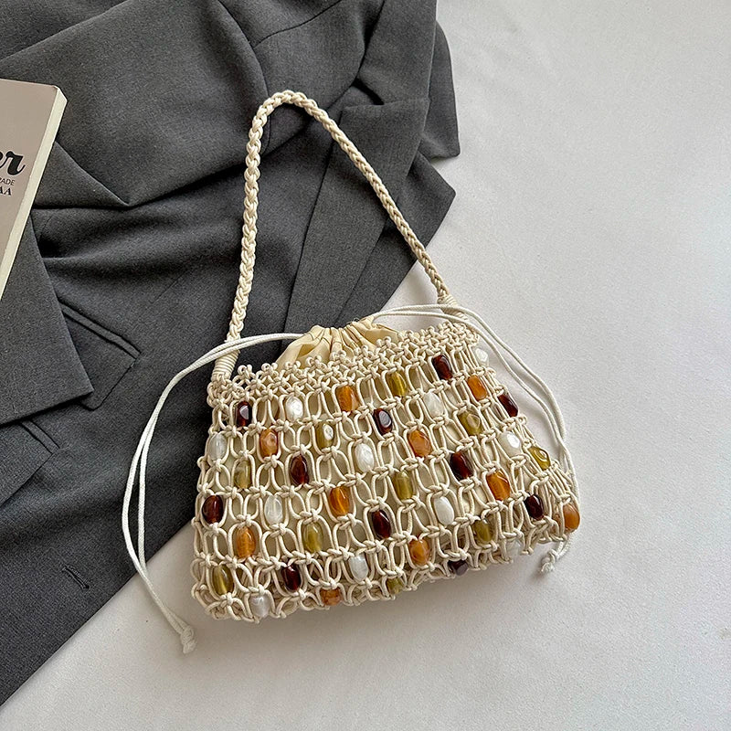 A cream macrame handbag with colorful stone accents, styled on a gray blazer over a white surface.