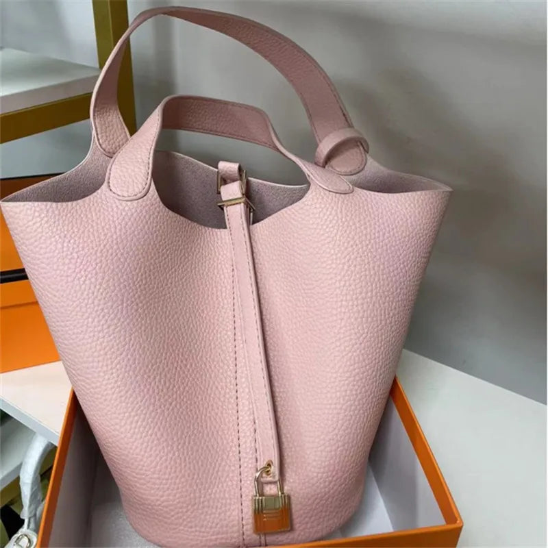 Pink handbag with a gold lock in an open box on a light gray background