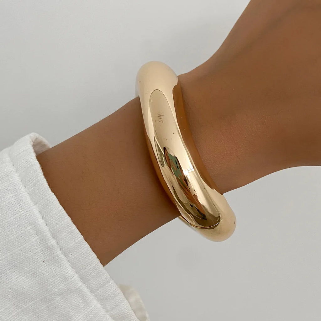 Gold bracelet on a wrist with a plain background