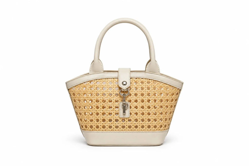 A structured handbag with a woven natural cane body and cream-colored faux leather trim, featuring dual top handles and a front turn-lock clasp with a hanging key charm, shown on a plain white background.