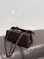Brown handbag with gold clasp on a gray surface