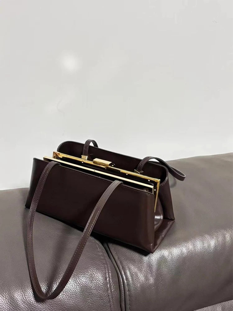 Brown handbag with gold clasp on a gray surface