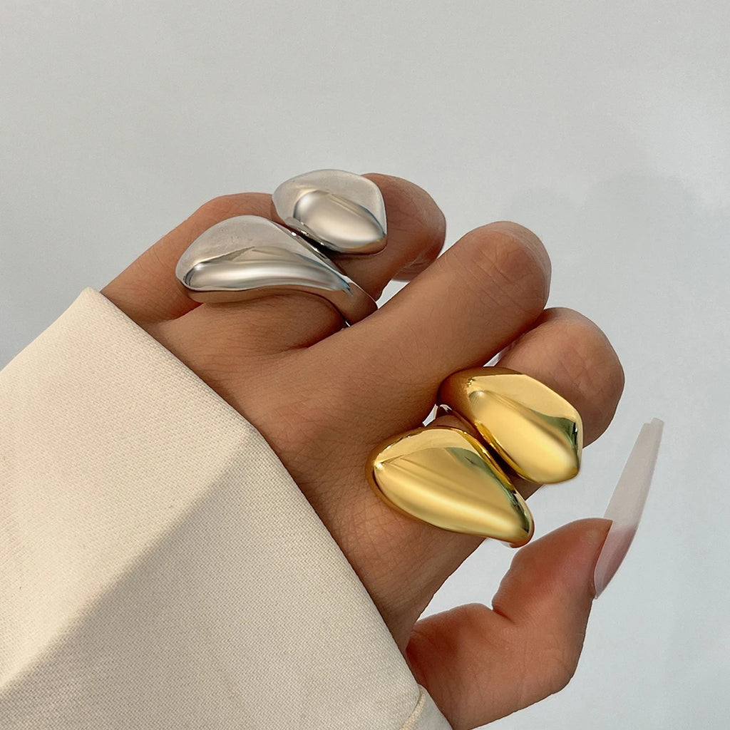 Hand wearing two rings, one gold and one silver, on a neutral background