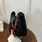 Black handbag with cherry and gold charm held by a hand on a wooden surface.