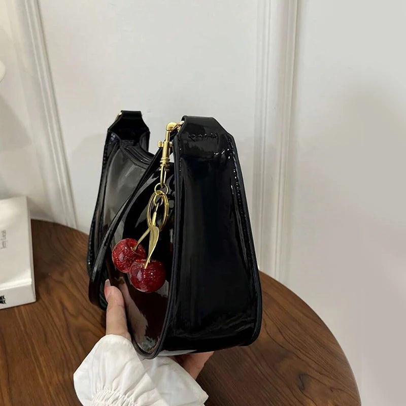 Black handbag with cherry and gold charm held by a hand on a wooden surface.