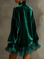 A woman wearing a dark green velvet turtleneck top with long sleeves and a ruffled lace hem, shown from the back against a neutral gray background.