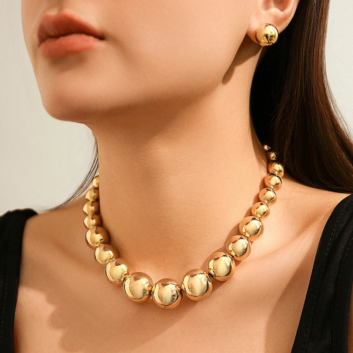 Gold necklace and earrings on a model against a neutral background