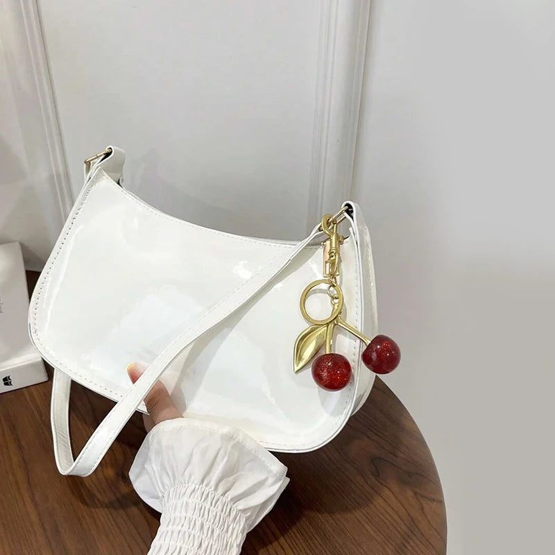 White handbag with a cherry keychain held by a hand on a wooden surface.