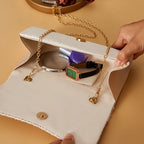 Beige clutch bag with gold chain handle, containing makeup items on a beige background