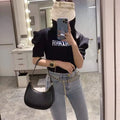 Person wearing a black 'AHAXA' t-shirt, light blue jeans, and a black handbag in a mirror selfie.