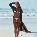 Woman in a black and white bikini with a black cover-up on a beach.