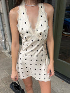 Woman wearing a white dress with black polka dots on a street.