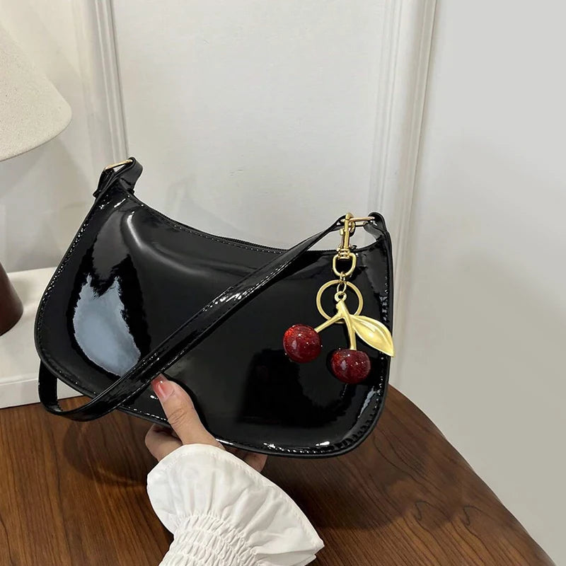 Black handbag with a cherry keychain held by a hand on a wooden surface.