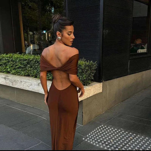 A woman wearing a brown off-the-shoulder maxi dress with a twist back design, standing on the sidewalk.