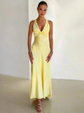 A woman wearing a yellow backless midi dress with a V-neckline and sleeveless top, standing against a plain background.