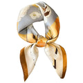 A beige, brown, white, and yellow floral patterned silk scarf tied in a bow.