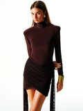 A woman wearing a brown turtleneck mini dress with long sleeves, standing against a white background.